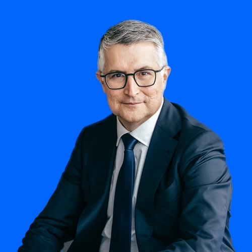 Santiago Argelich Hesse im dunklen Anzug vor blauem Hintergrund.