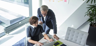 Mann und Frau im Büro in Businesskleidung sprechen vor Laptop.