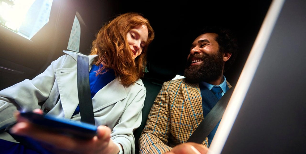 Mann und Frau sitzen im Auto und halten jeweils ein Smartphone.